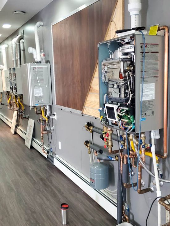 A series of tankless water heaters installed along a wall in a commercial setting, each with detailed pipework and controls.