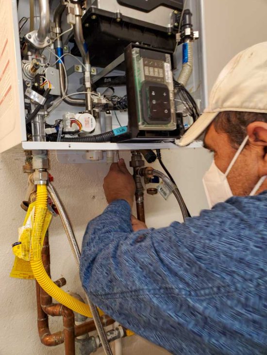 Technician adjusting valves on a modern water heater, showing intricate pipework and digital control units.