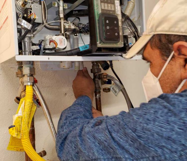 Technician adjusting valves on a modern water heater, showing intricate pipework and digital control units.