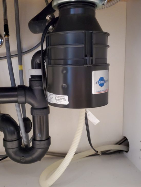 Compact black InSinkErator garbage disposal installed under a sink, neatly integrated with the kitchen plumbing.