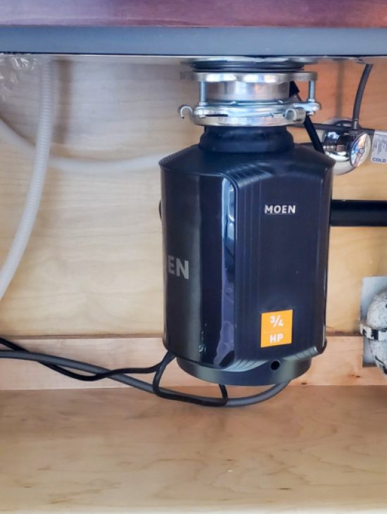 Black Moen garbage disposal unit installed under a kitchen sink, connected to the plumbing system.