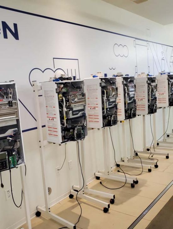 A row of exposed Navien water heaters on stands in a training facility, showcasing the internal components.