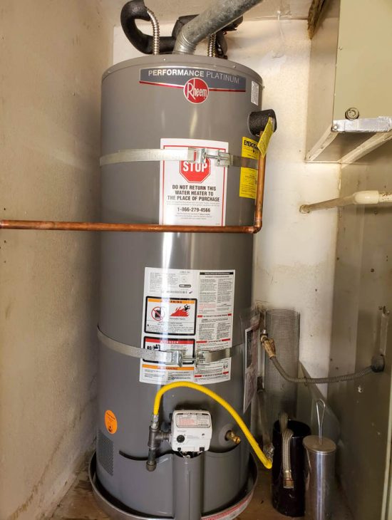 Rheem Performance Platinum water heater installed in a utility area, complete with safety stickers and gas connection.