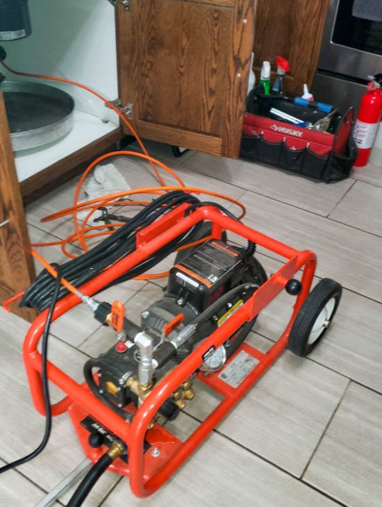 Compact hydro-jetting machine placed on a bathroom floor, equipped with hoses and fittings, illustrating modern plumbing tools in use.