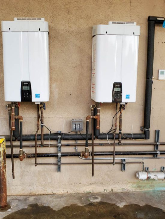 Two high-capacity tankless water heaters installed on a wall, efficiently set up with multiple copper pipes and digital temperature controls.