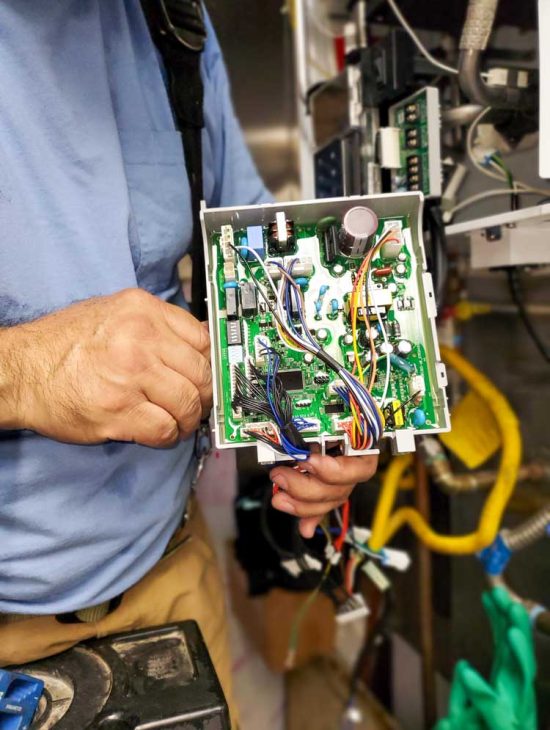 Close-up of a technician's hands working on the electronic circuit board of a boiler, highlighting complex wiring.