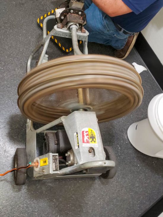 Industrial drain cleaning machine in operation with a rotating drum, used by a professional plumber during a service call.