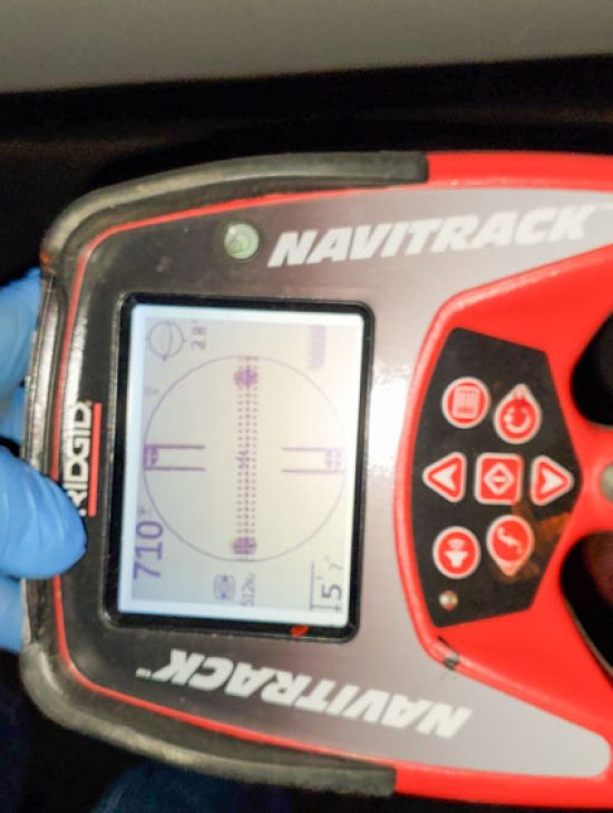 Hand holding a RIDGID Navitrack precision pipe locator, demonstrating technology used for detecting underground pipes.