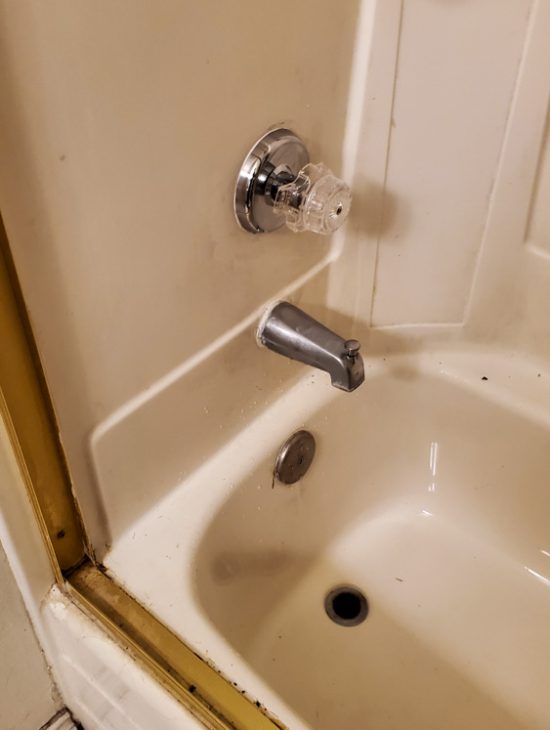Standard white shower stall with basic plumbing fixtures, showing signs of wear and needing potential upgrades.