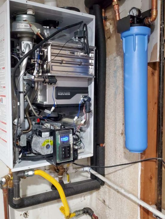Navien tankless water heater installed in a basement with a blue water filtration unit, showcasing a clean and organized setup.