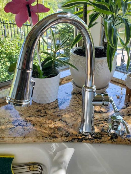 Modern stainless steel faucet over a kitchen sink with a view of a window, showcasing a clean and stylish interior.