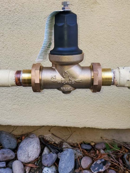 Close-up of a water pressure regulator with a gauge installed on an outdoor water pipeline.