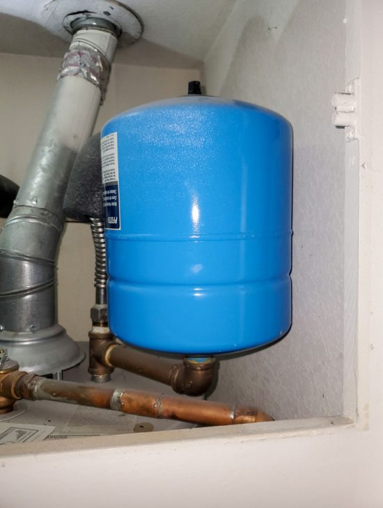 Blue pressure tank installed under a utility sink, connected to a water filtration system.
