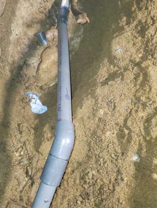 A damaged water pipe partially buried in sandy soil, with repair sections visible.