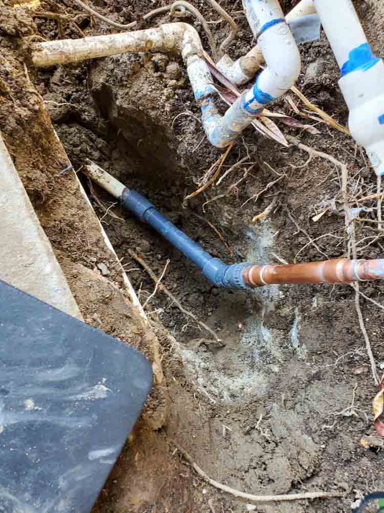 A trench dug in the ground revealing blue and white pipes for plumbing repair.