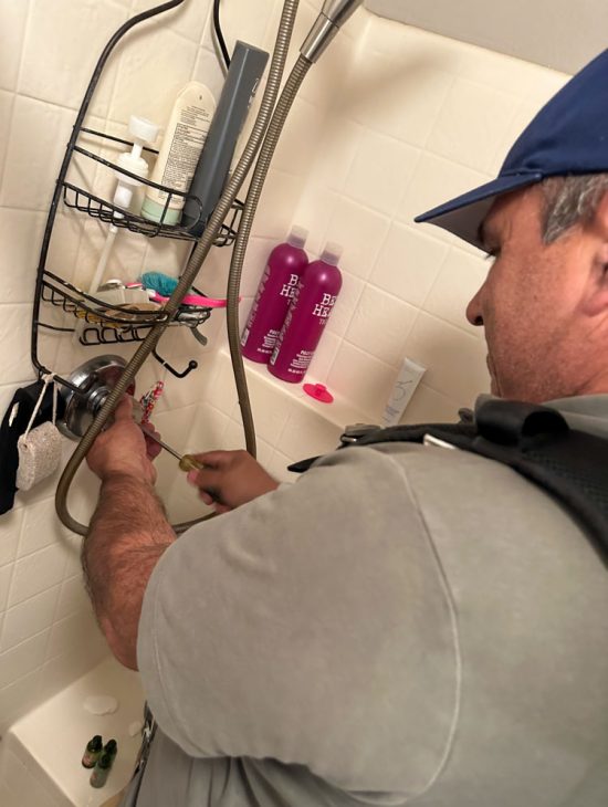 Plumber adjusting a shower fixture in a residential bathroom, surrounded by various bath products.