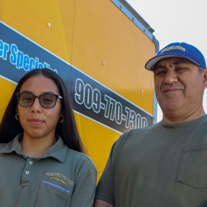 A father-daughter duo of plumbers posing in front of their company vehicle, emphasizing their professionalism and team dynamics in the plumbing industry.