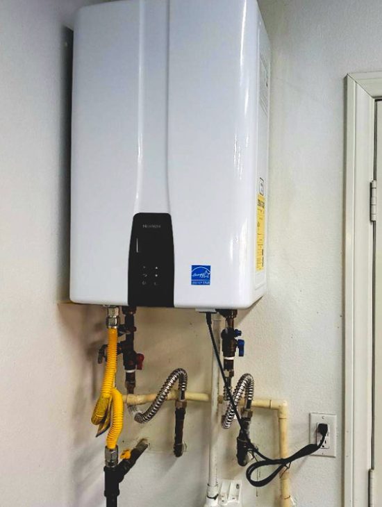 Sleek white tankless water heater installed against a textured wall with multiple connected pipes and cables.
