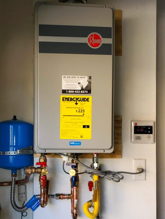 Modern Rheem tankless water heater installed in a utility room with energy guide and contact information displayed.